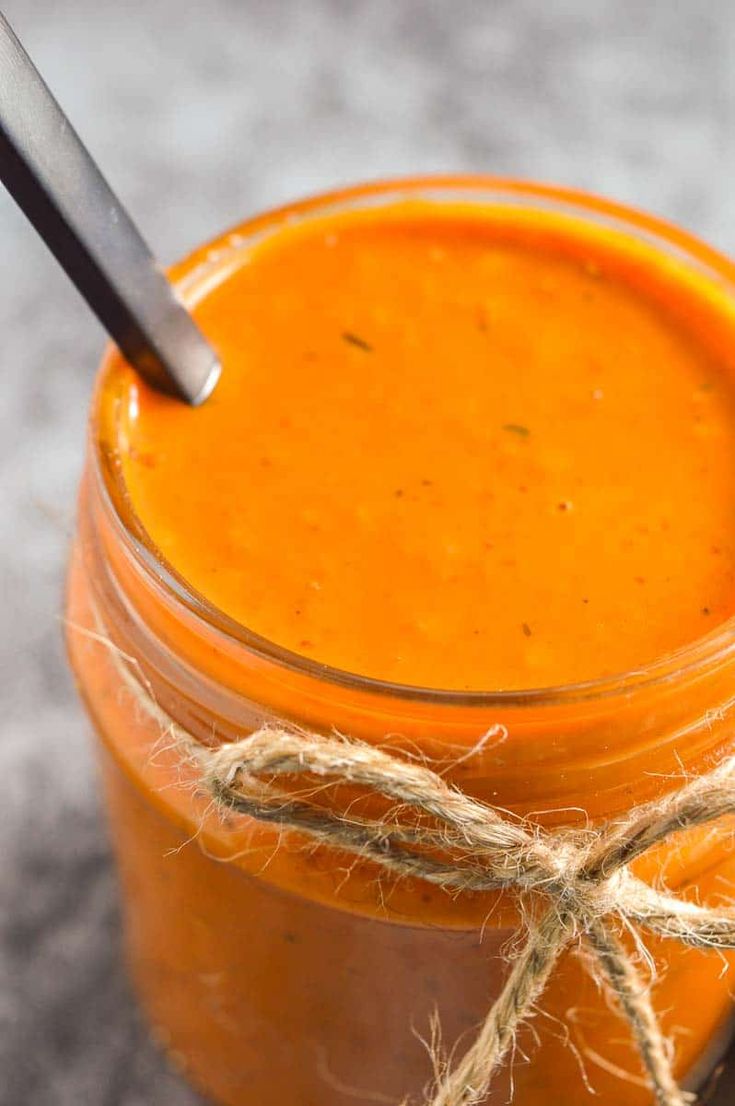A jar of duo pepper sauce with a spoon inside, tied with a twine and placed on a textured surface.
